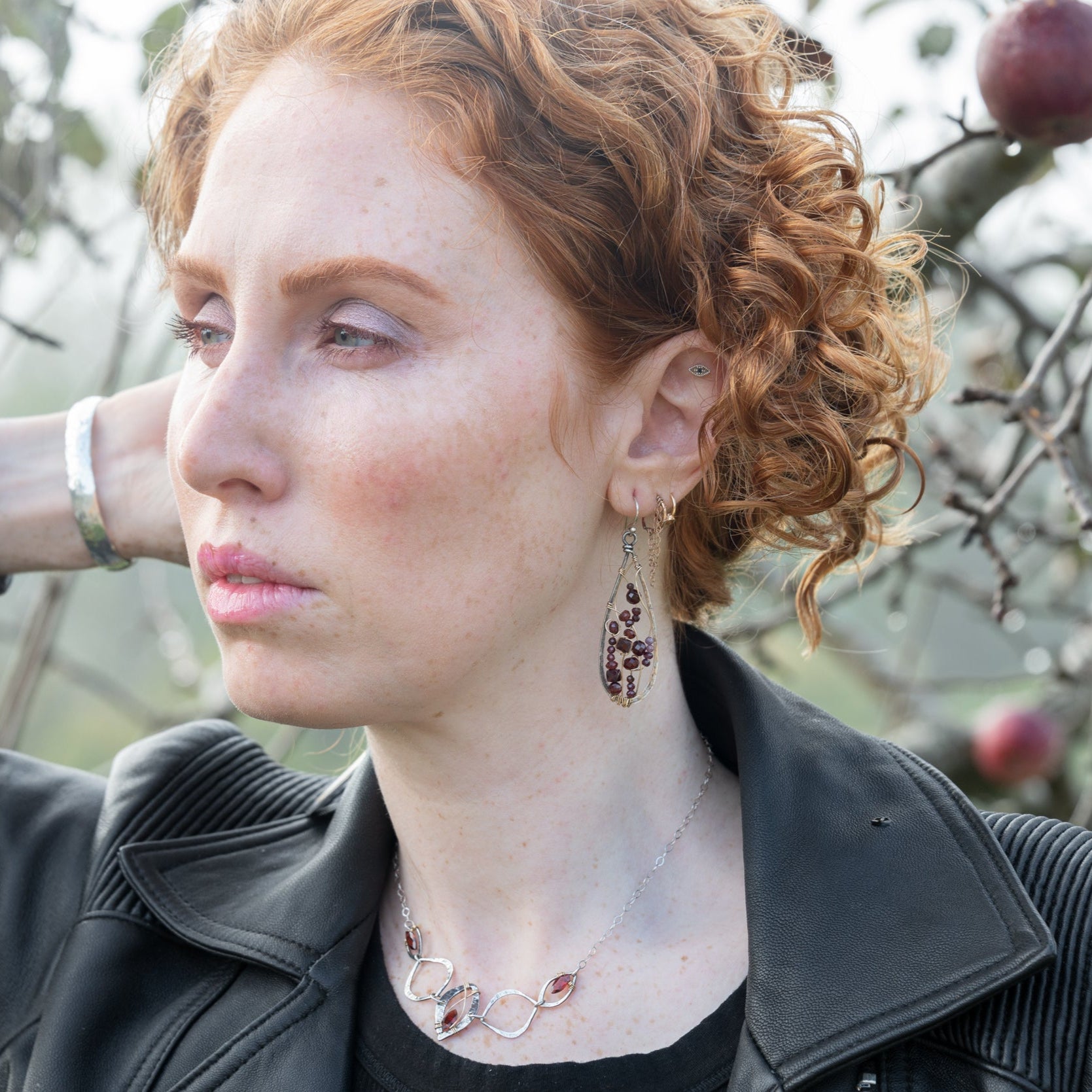 Woman with red hair and garnet earrings standing in front of an apple tree
