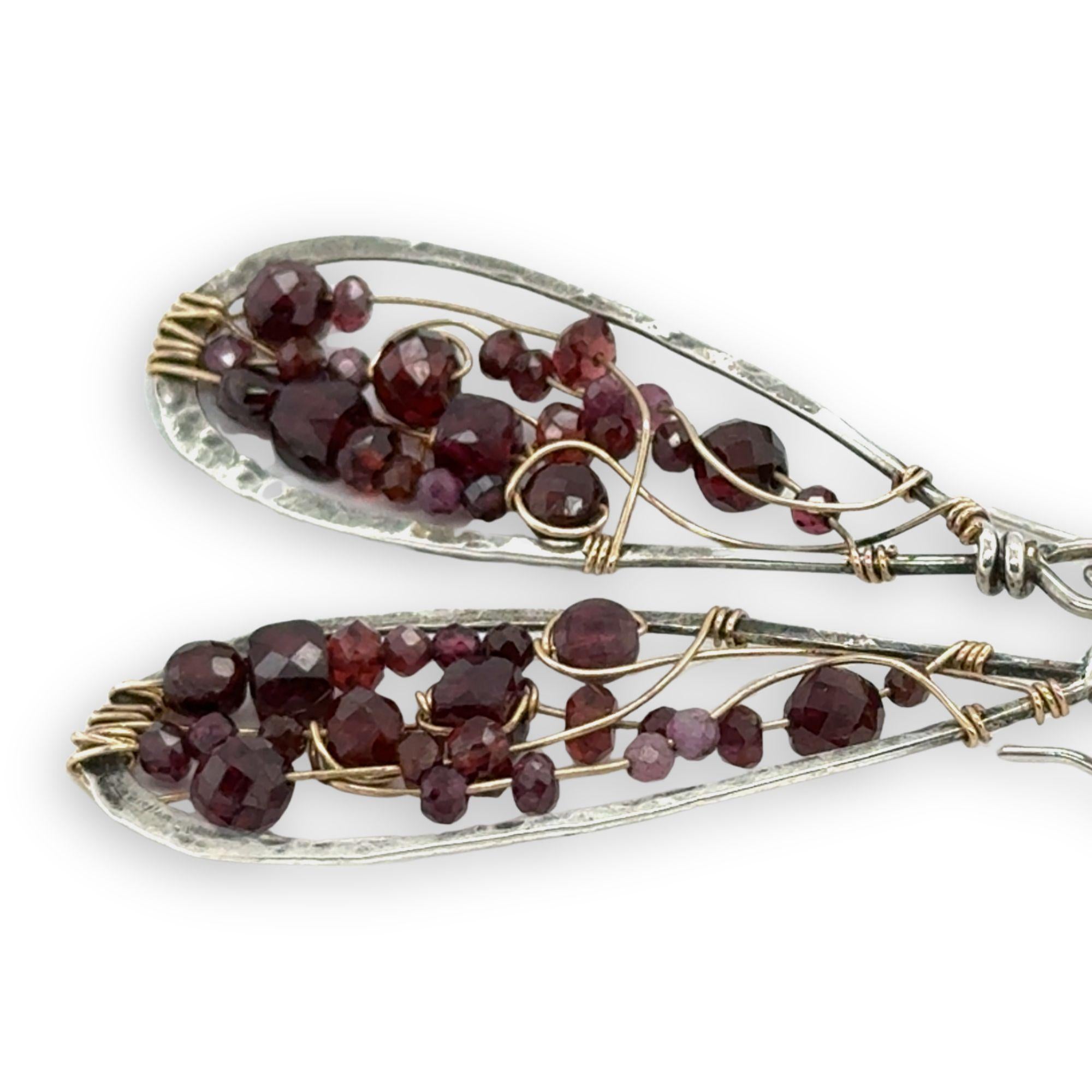 Teardrop-shaped earrings with garnet beads and gold wirework on a white background