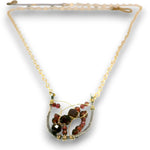 A gold chain necklace with a unique crescent-shaped pendant featuring faceted dark red and brown beads wrapped in gold wire, set against a plain white background.