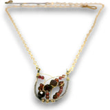 A gold chain necklace with a unique crescent-shaped pendant featuring faceted dark red and brown beads wrapped in gold wire, set against a plain white background.