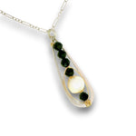 A teardrop-shaped pendant necklace featuring a silver-toned chain, a clear glass or resin outer frame, dark green faceted gemstones, and a central white cabochon stone with a gold accent.