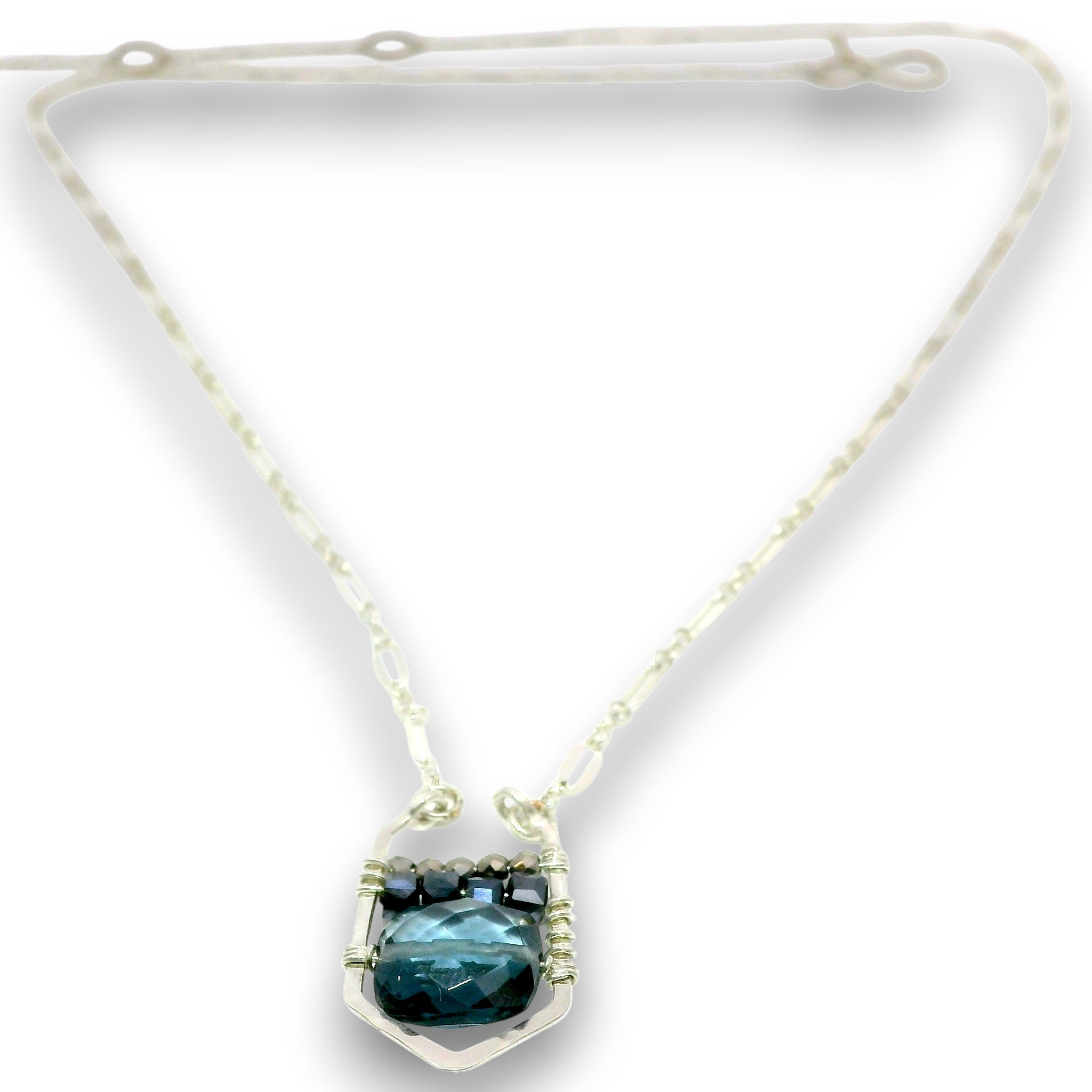 A silver-toned necklace featuring a textured chain and a central pendant with a faceted dark teal-blue gemstone held in a silver setting with small dark accent stones, shown on a white background.