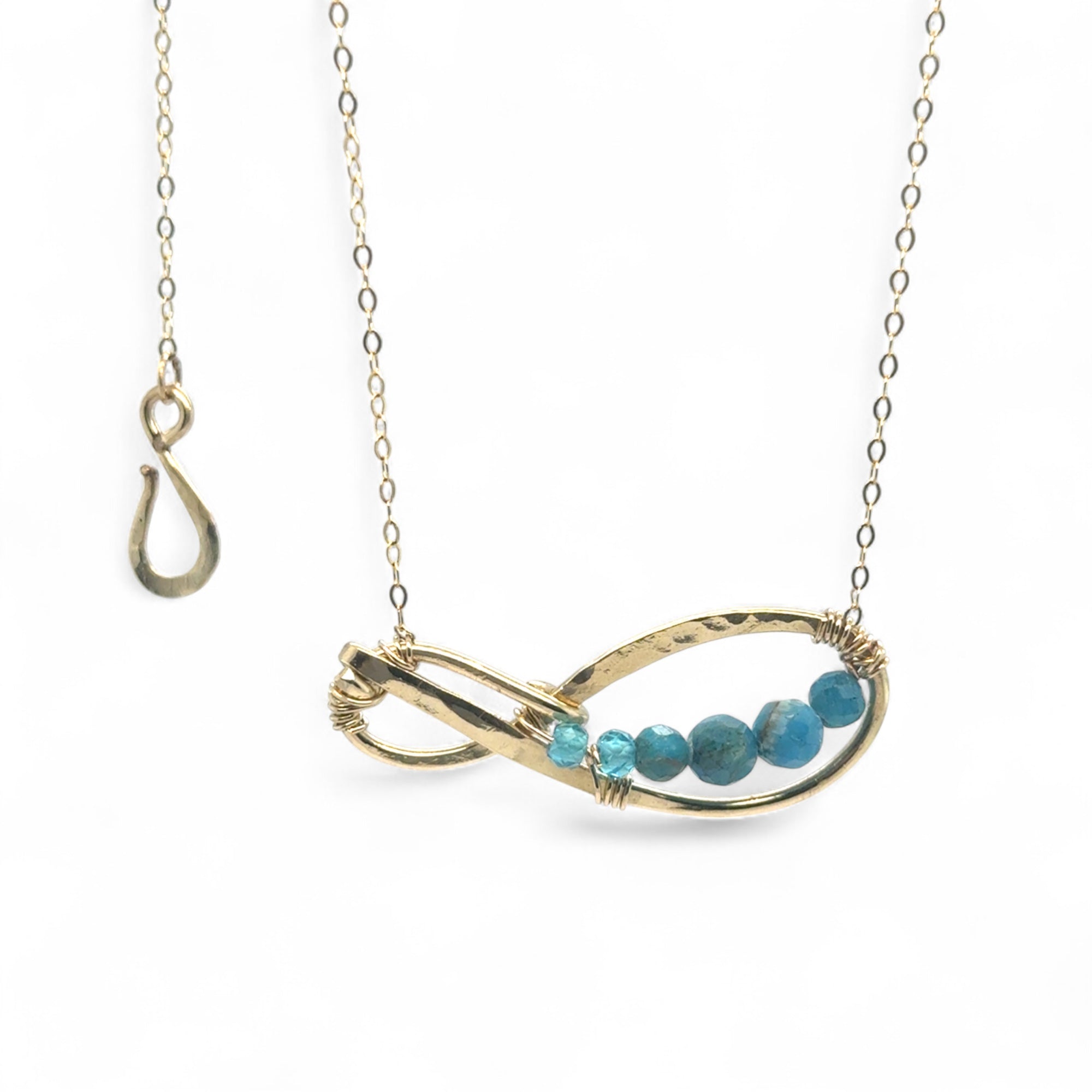 A brass infinity-shaped pendant necklace with blue faceted gemstones on the inside, attached to a gold-filled chain with an adjustable clasp.