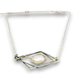 A silver-toned geometric pendant necklace featuring a central baroque pearl wrapped with delicate gold wire, suspended on a fine silver chain against a white background.