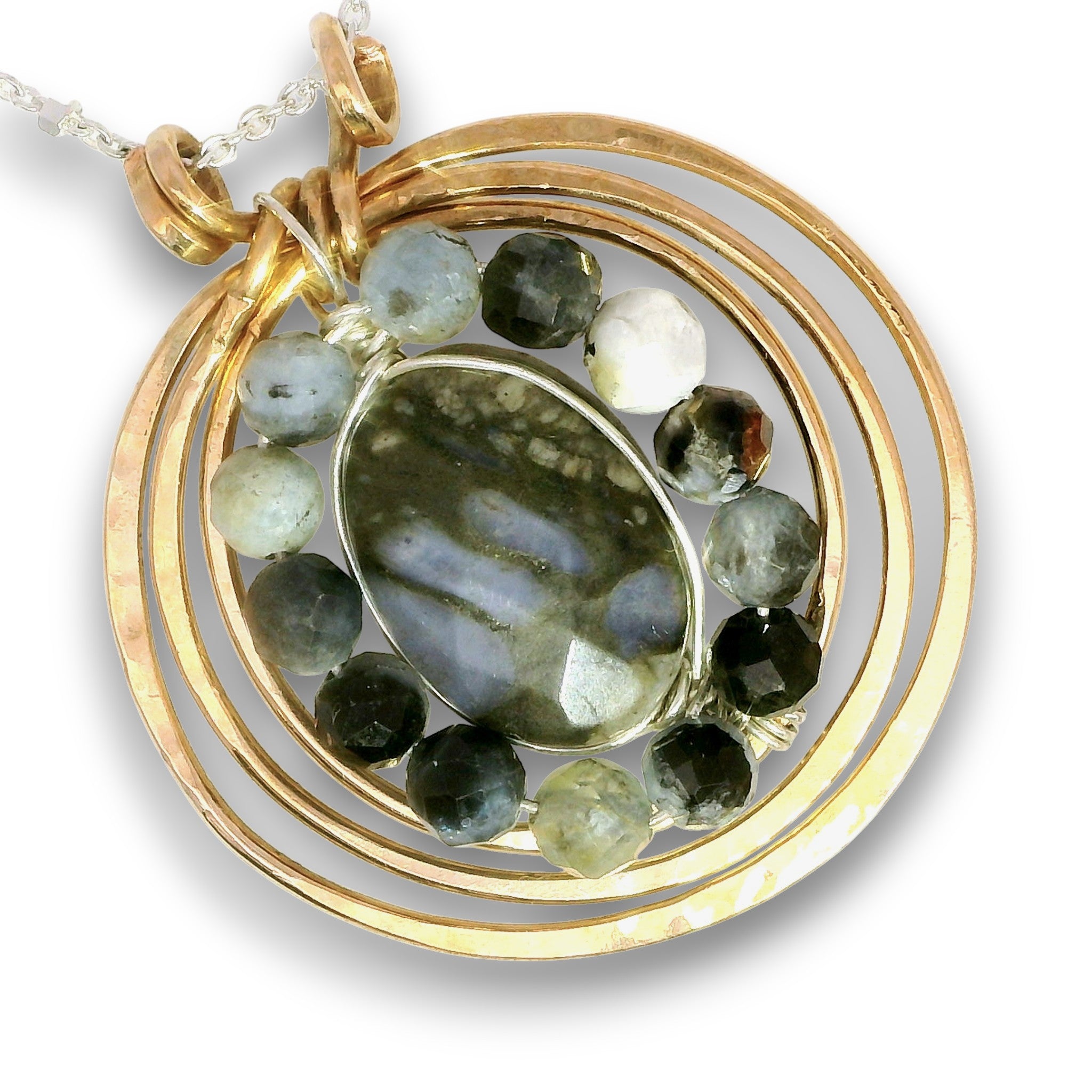 A gold pendant necklace featuring a central oval labradorite stone surrounded by a ring of faceted dark gray, black, and white beads, with textured gold concentric circles and a silver-toned chain.