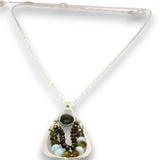 A silver-toned triangle pendant necklace featuring a dark green oval stone and layered beaded strands in brown, gold, and light blue, suspended on a delicate silver chain.