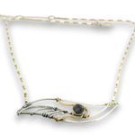A delicate wire-wrapped necklace featuring a central dark gray stone, crafted with both silver and gold-toned metal wires on a white background.