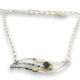 A delicate wire-wrapped necklace featuring a central dark gray stone, crafted with both silver and gold-toned metal wires on a white background.