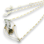 A delicate handmade wire-wrapped necklace featuring a silver and gold geometric pendant with a dark gray stone, shown on a clean white background.