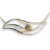 A handmade wave-shaped necklace featuring hammered silver-toned metal, gold-toned wire wrapping, and a central round gray stone, shown on a plain white background.