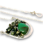A silver wire-wrapped necklace featuring a large green stone pendant and smaller dark green and metallic green beads, shown on a white background.