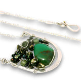 A silver wire-wrapped necklace featuring a large green stone pendant and smaller dark green and metallic green beads, shown on a white background.