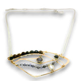 A gold-toned geometric necklace with a white adjustable cord, featuring dark green and brown beads, a row of gray beads, and a central clear teardrop gemstone.