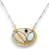 A gold pendant necklace featuring a double oval frame with a beige oval stone, a light blue marquise-shaped stone, and a small black round stone, suspended from a silver-toned chain on a white background.