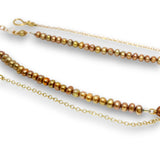 A strand of iridescent freshwater pearl beads in shades of bronze, gold, and copper, threaded onto a delicate gold chain with a lobster clasp and extension cord, shown on a white background.