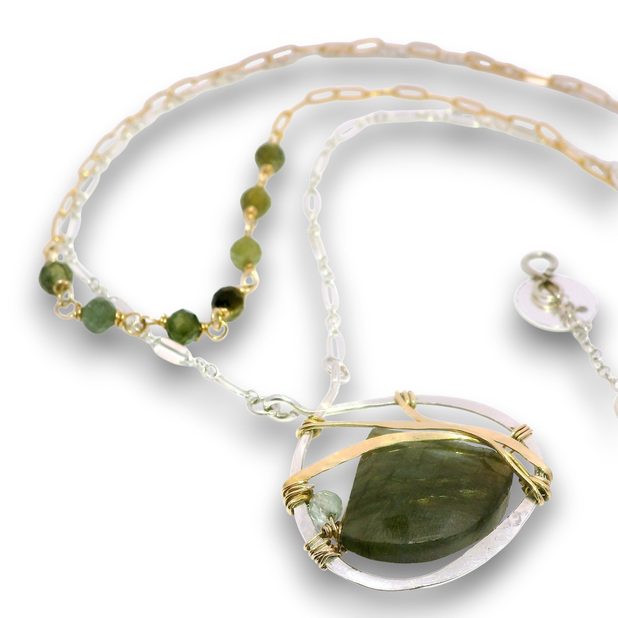 A delicate necklace featuring a large oval pendant with a dark green stone wrapped in gold wire, a clear glass border, and a silver chain. The necklace also includes a beaded section with small green beads and gold links.