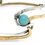 A sterling silver and brass hammered cuff bracelet featuring a single blue amazonite gemstone, with a twist design and an interlocked structure.