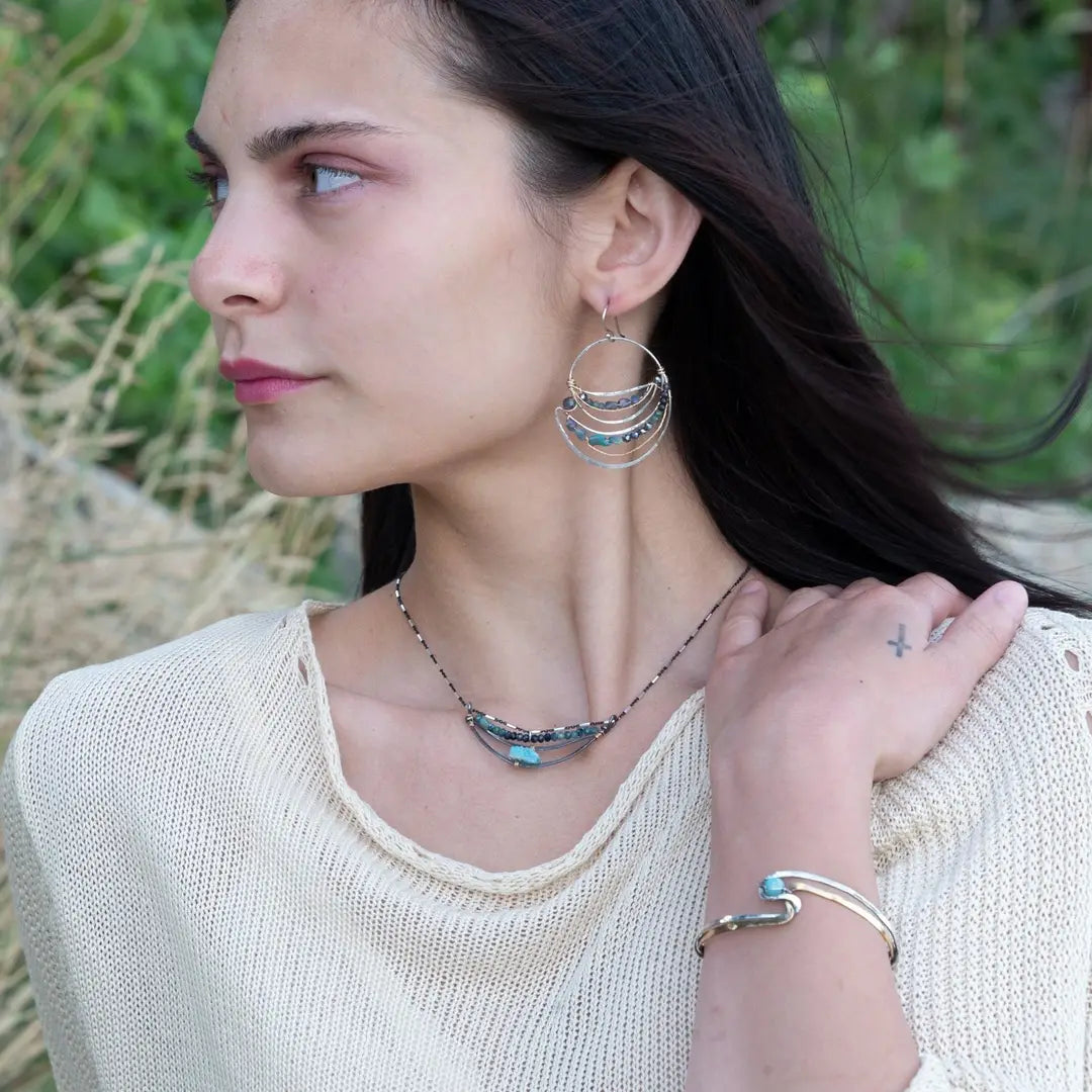 A sterling silver and brass hammered cuff bracelet featuring a single blue amazonite gemstone, with a twist design and an interlocked structure.
