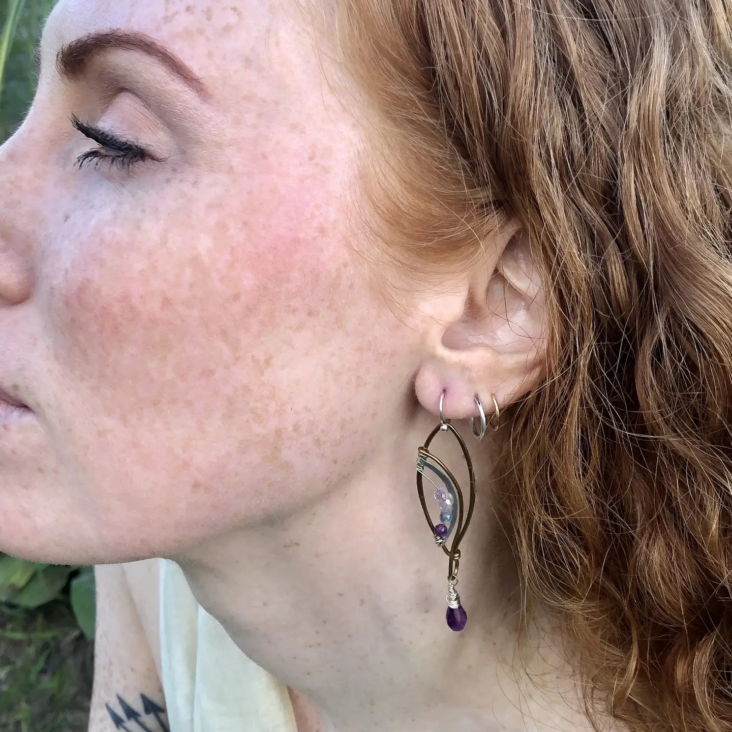 Faceted amethyst drops hang from a brass marquise earring with hammered sterling silver arches and faceted fluorite gemstones