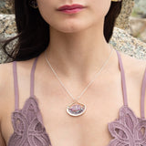 A sterling silver adjustable chain necklace with a hammered handmade brass pendant featuring a glowing amethyst smooth pebble, surrounded by faceted blue zoisite and micro faceted lavender cubic zirconia gemstones.