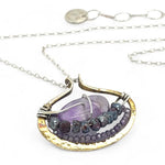 A sterling silver adjustable chain necklace with a hammered handmade brass pendant featuring a glowing amethyst smooth pebble, surrounded by faceted blue zoisite and micro faceted lavender cubic zirconia gemstones.