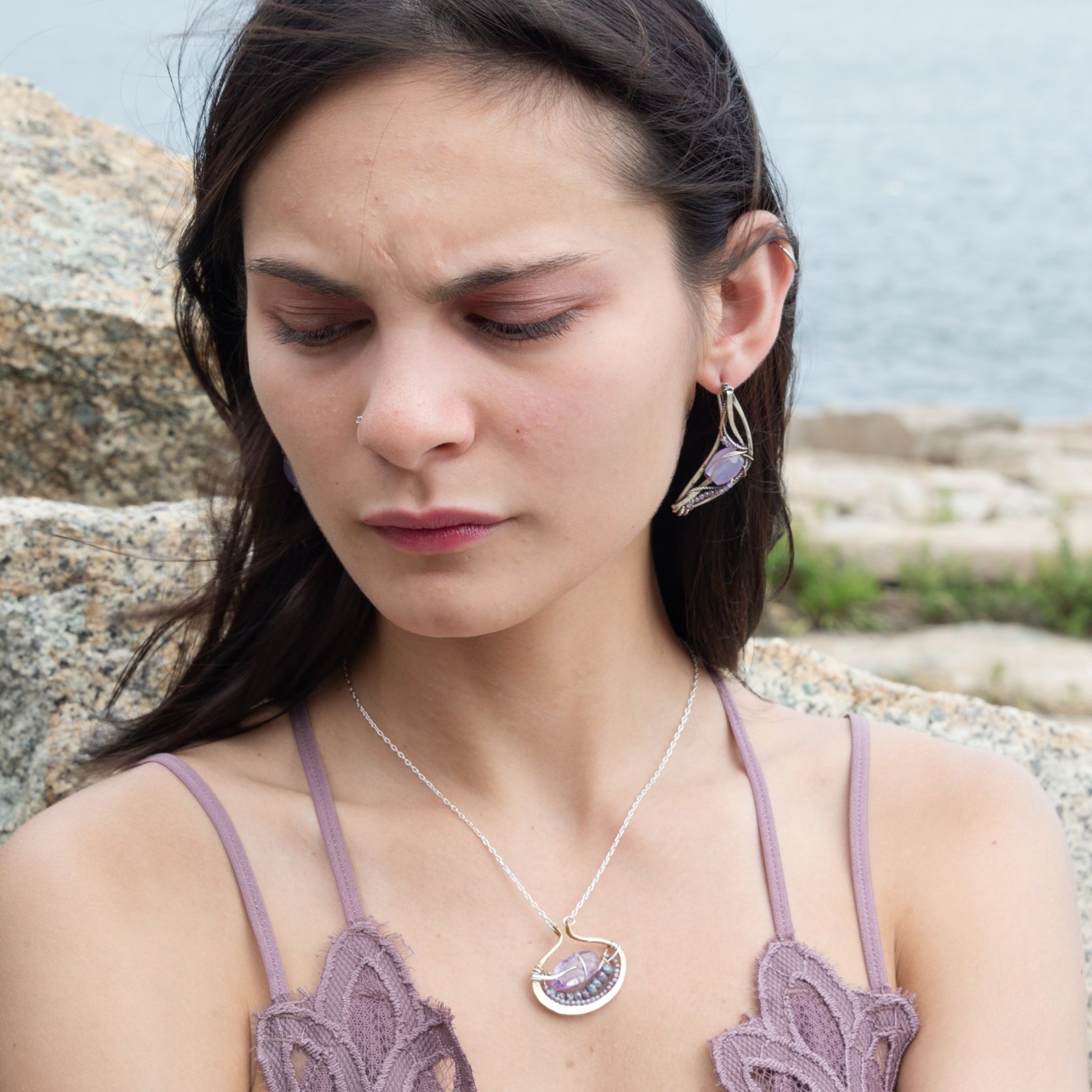 A sterling silver adjustable chain necklace with a hammered handmade brass pendant featuring a glowing amethyst smooth pebble, surrounded by faceted blue zoisite and micro faceted lavender cubic zirconia gemstones.