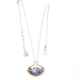 A sterling silver adjustable chain necklace with a hammered handmade brass pendant featuring a glowing amethyst smooth pebble, surrounded by faceted blue zoisite and micro faceted lavender cubic zirconia gemstones.