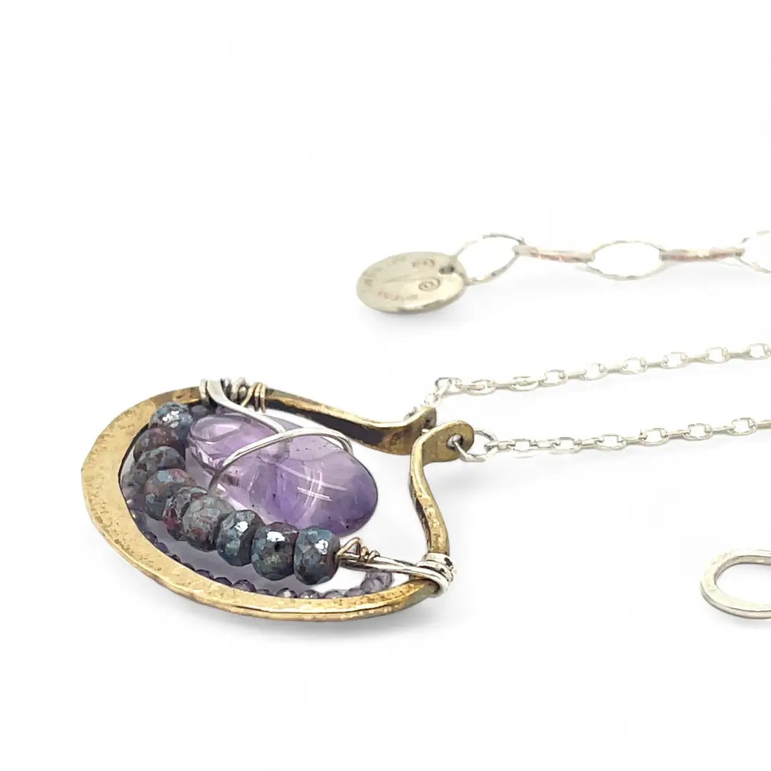 A sterling silver adjustable chain necklace with a hammered handmade brass pendant featuring a glowing amethyst smooth pebble, surrounded by faceted blue zoisite and micro faceted lavender cubic zirconia gemstones.