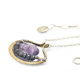 A sterling silver adjustable chain necklace with a hammered handmade brass pendant featuring a glowing amethyst smooth pebble, surrounded by faceted blue zoisite and micro faceted lavender cubic zirconia gemstones.