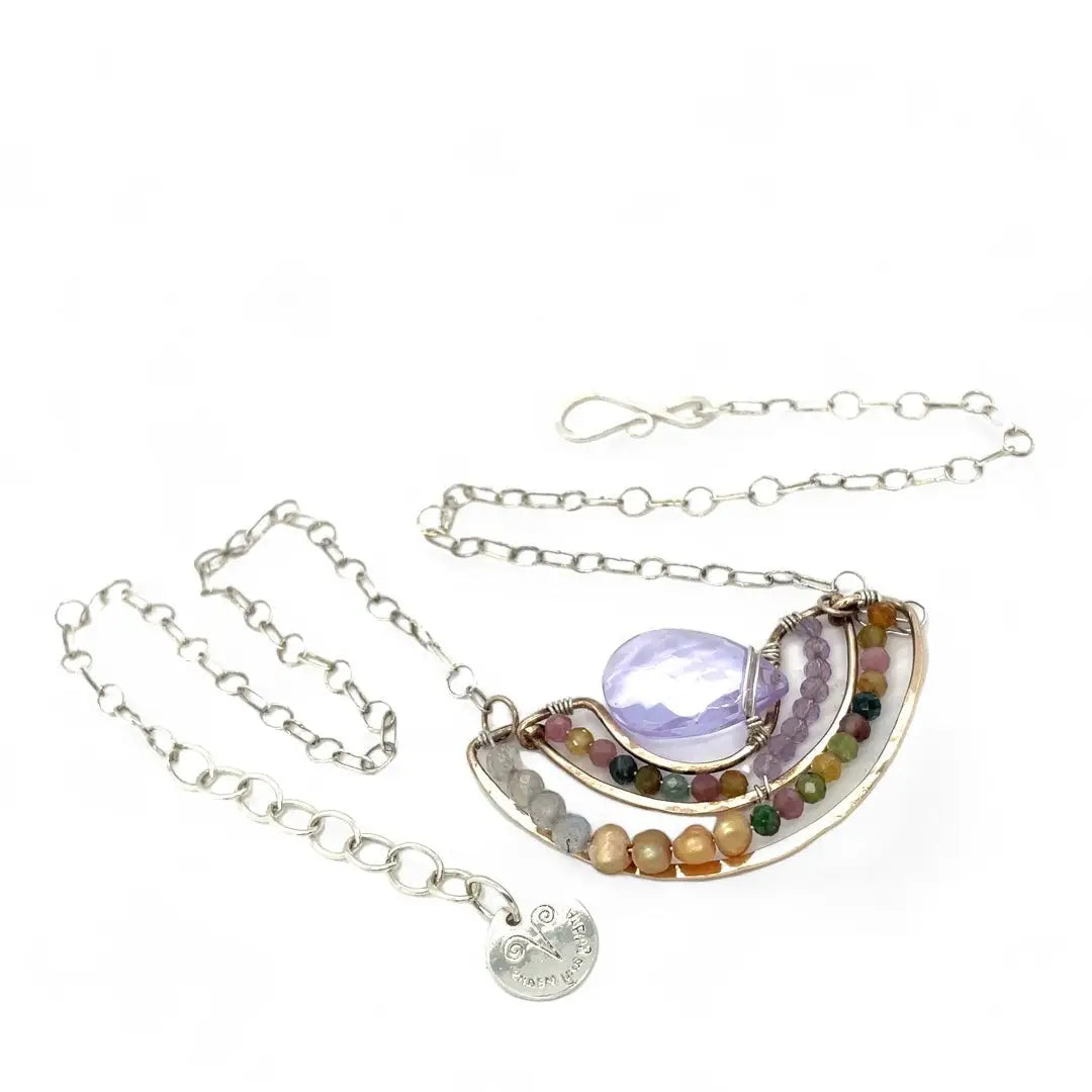 A handmade bronze necklace featuring a layered design with a faceted teardrop-shaped lavender quartz, tourmaline, amethyst, and labradorite gemstones, accompanied by golden fresh water with an adjustable chain and a signature clasp.
