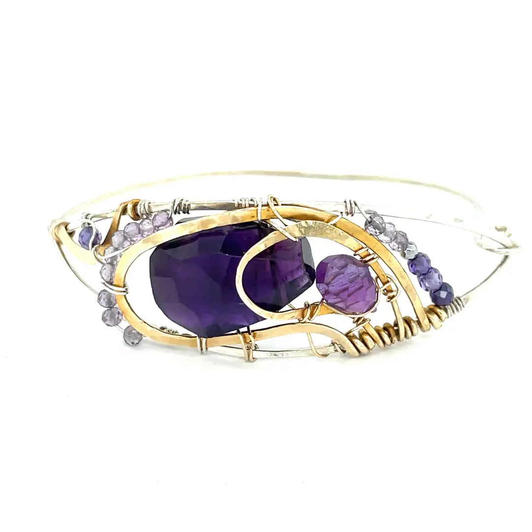 A handcrafted sterling silver bracelet featuring a faceted drop of dark amethyst and other amethyst gemstones in hammered brass, accompanied by micro-faceted cubic zirconia