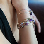 A collection of faceted amethyst nuggets, pink sapphire, and ruby gemstones are wrapped in gold filled wire onto a bracelet formed of leaf stamped oxidized sterling, bright sterling, and bronze hammered waves