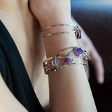 A collection of faceted amethyst nuggets, pink sapphire, and ruby gemstones are wrapped in gold filled wire onto a bracelet formed of leaf stamped oxidized sterling, bright sterling, and bronze hammered waves