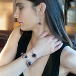 A collection of faceted amethyst nuggets, pink sapphire, and ruby gemstones are wrapped in gold filled wire onto a bracelet formed of leaf stamped oxidized sterling, bright sterling, and bronze hammered waves