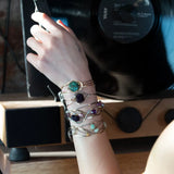 A collection of faceted amethyst nuggets, pink sapphire, and ruby gemstones are wrapped in gold filled wire onto a bracelet formed of leaf stamped oxidized sterling, bright sterling, and bronze hammered waves