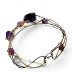 A collection of faceted amethyst nuggets, pink sapphire, and ruby gemstones are wrapped in gold filled wire onto a bracelet formed of leaf stamped oxidized sterling, bright sterling, and bronze hammered waves