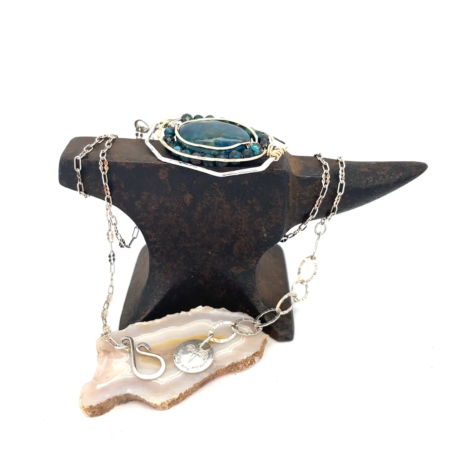 A sterling silver necklace featuring a large, oval-shaped teal apatite gemstone encircled by smaller faceted chrysocolla gemstones, set in gold-filled and bronze accents, displayed on a silver chain.