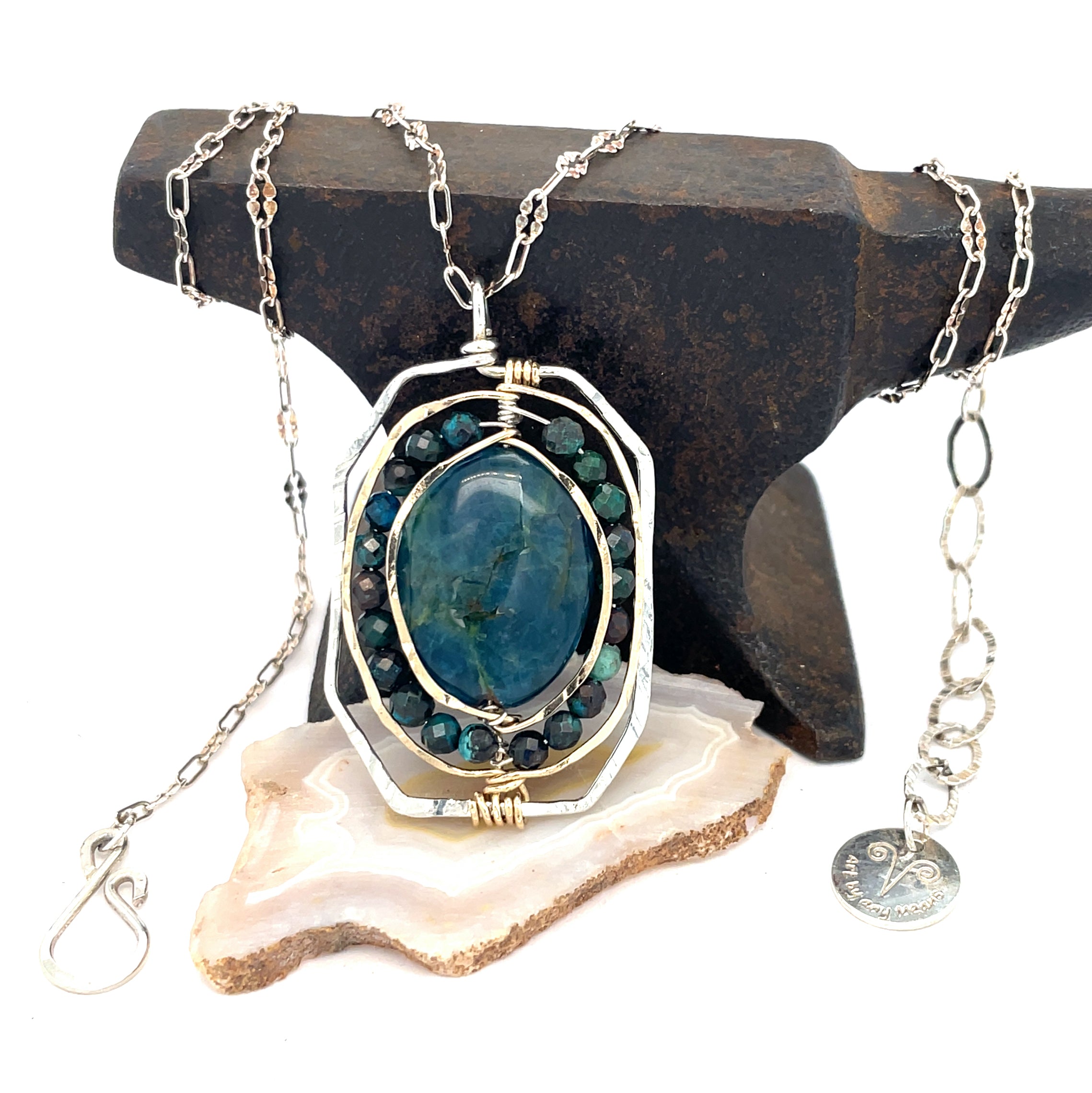 A sterling silver necklace featuring a large, oval-shaped teal apatite gemstone encircled by smaller faceted chrysocolla gemstones, set in gold-filled and bronze accents, displayed on a silver chain.
