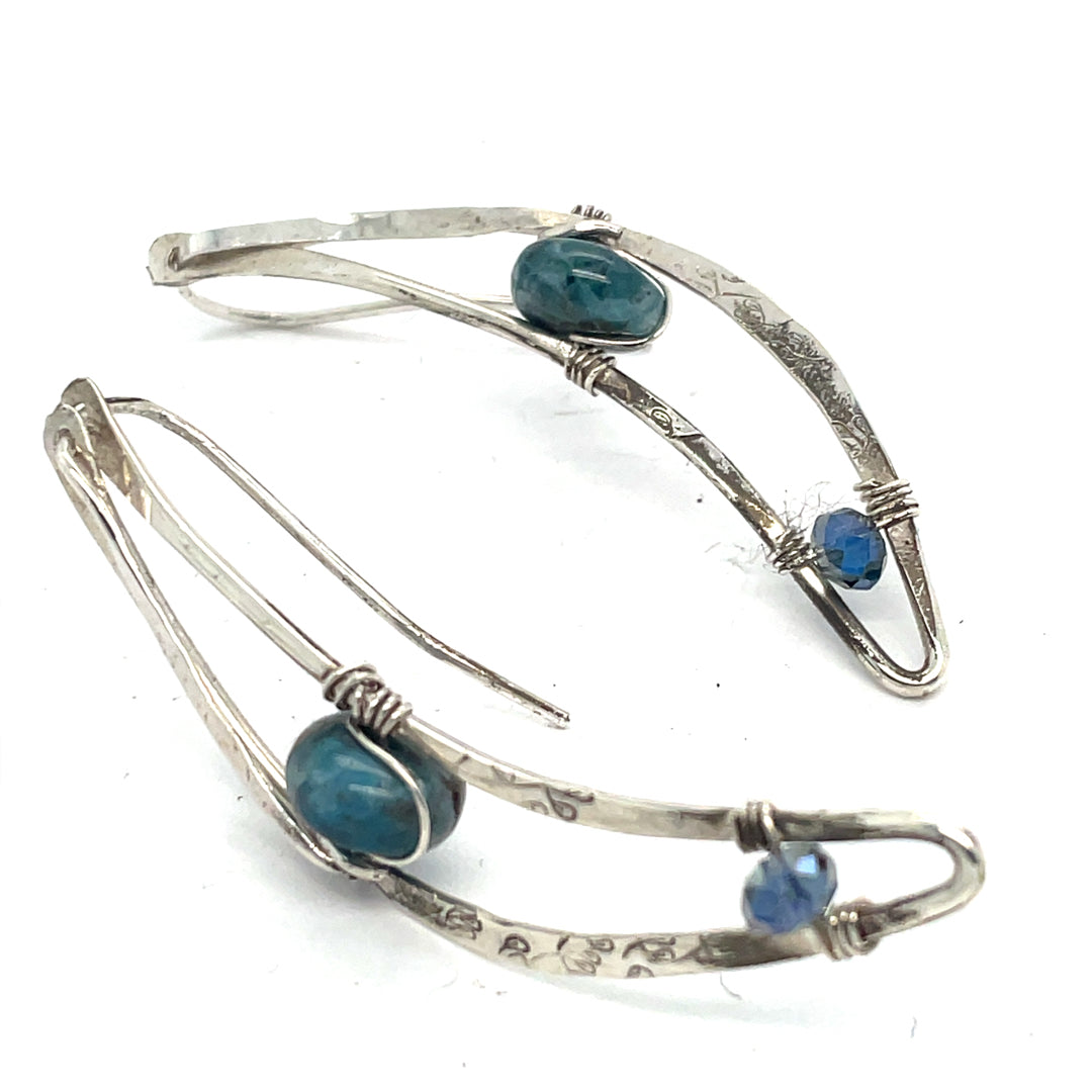 A pair of crescent earrings with hammered oxidized sterling silver and blue apatite gemstones set in the center.