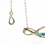 A brass infinity-shaped pendant necklace with blue faceted apatite and opal gemstones on the inside, attached to a gold-filled chain with an adjustable clasp.