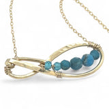 A brass infinity-shaped pendant necklace with blue faceted apatite and opal gemstones on the inside, attached to a gold-filled chain with an adjustable clasp.