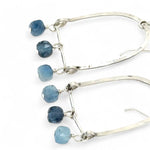 A pair of sterling silver arch earrings with faceted aquamarine gemstones attached to the bottom