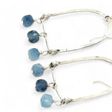 A pair of sterling silver arch earrings with faceted aquamarine gemstones attached to the bottom