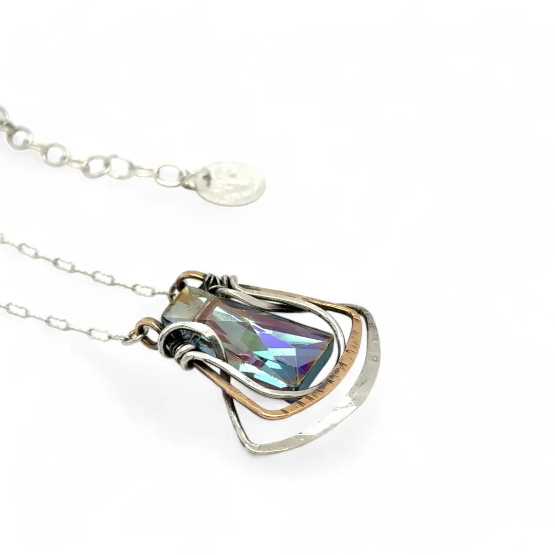 A blue/purple rectangular crystal is held in layers of sterling silver and bronze hammered wire pendant on sterling silver delicate chain necklace