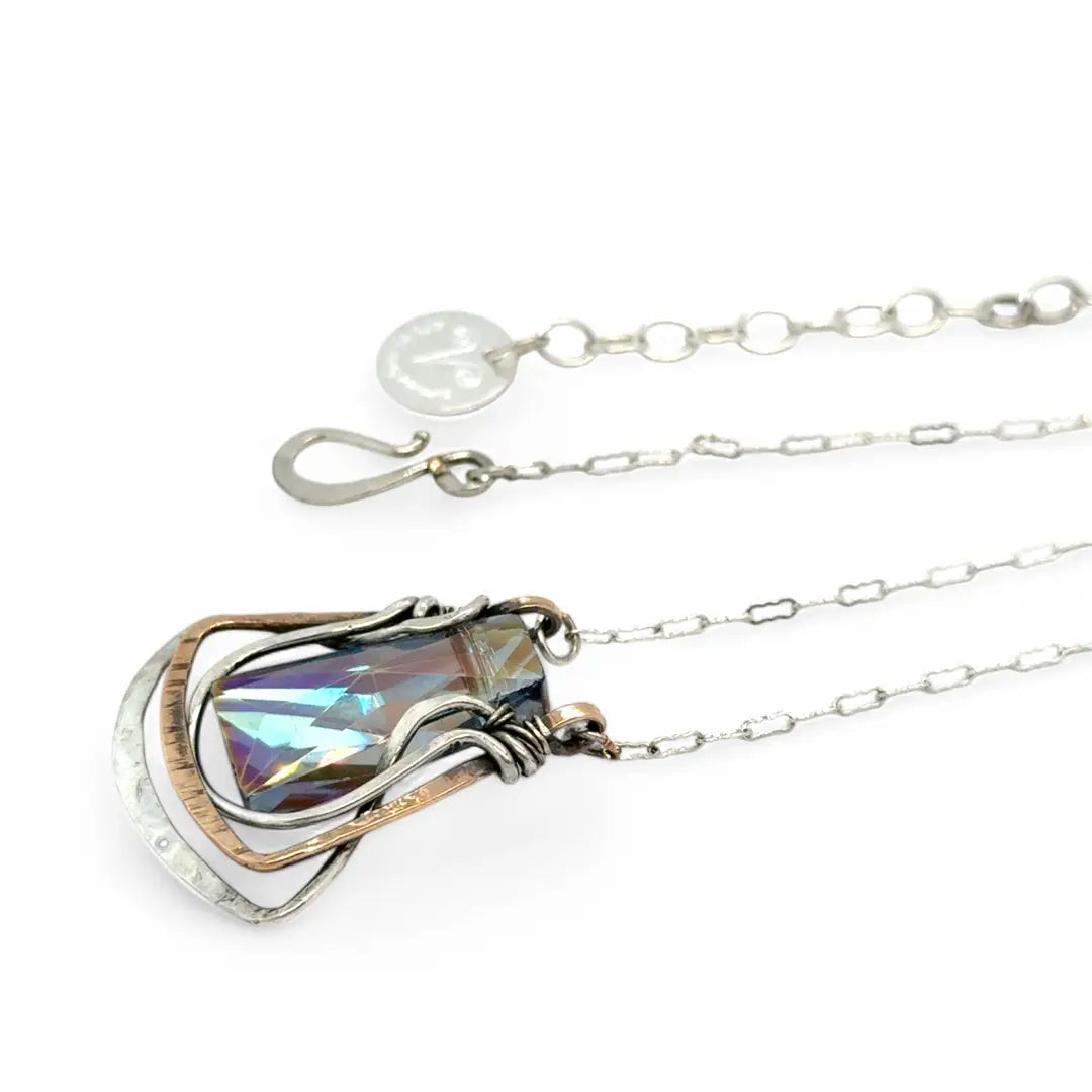 A blue/purple rectangular crystal is held in layers of sterling silver and bronze hammered wire pendant on sterling silver delicate chain necklace