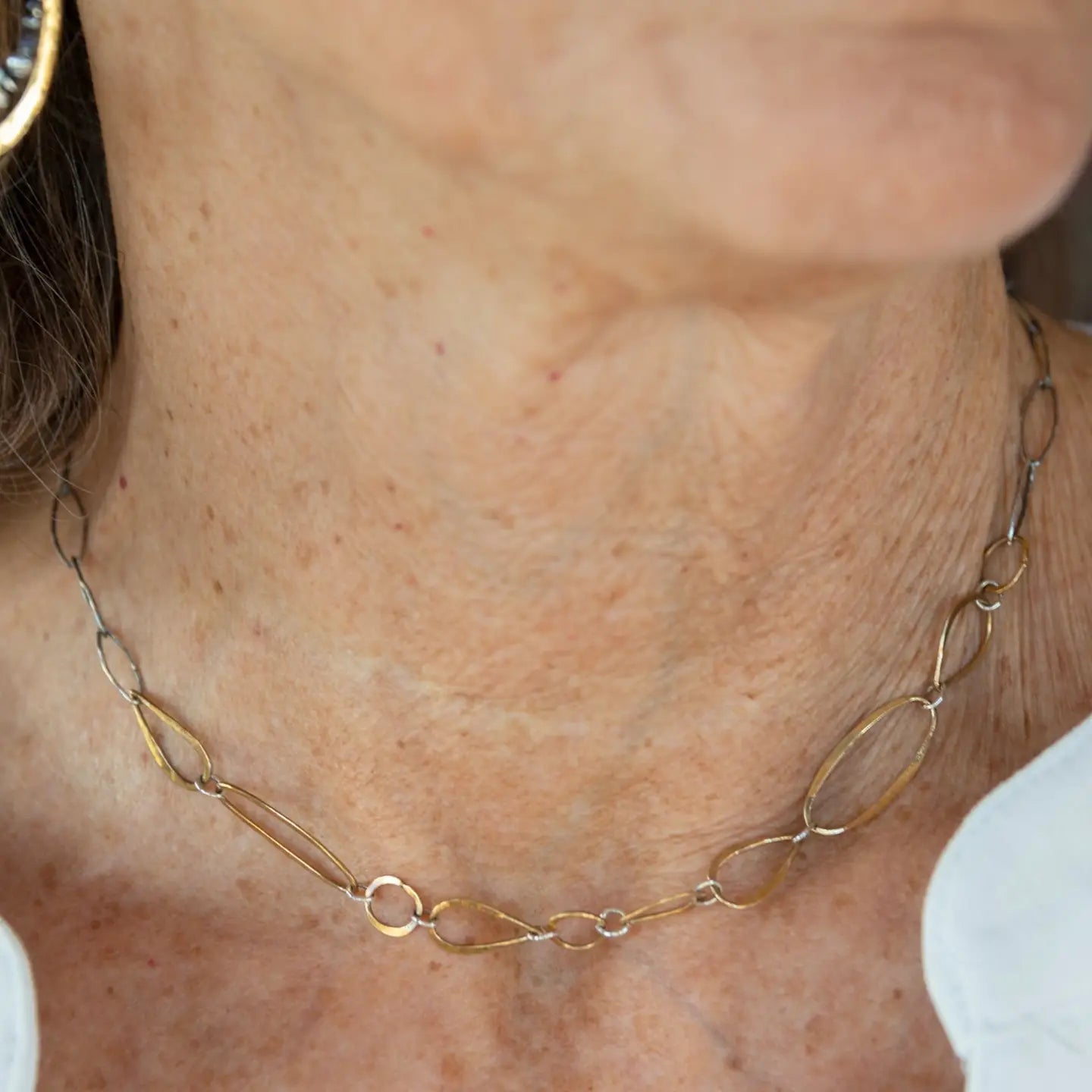 An artisanal chain necklace with a combination of handmade hammered brass links and open diamond cut oxidized sterling links 