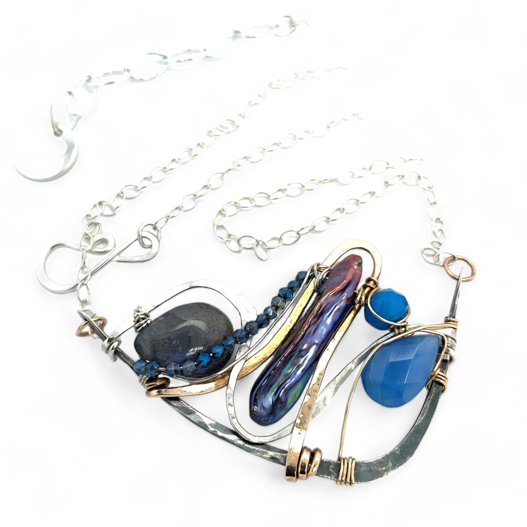 Darkened sterling silver boomerang shaped pendant necklace with waves of hammered bronze, sterling silver, and gold filled wire holding smooth labradorite, blue jade, blue crystal, and a purple fresh water stick pearl in place