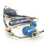 Darkened sterling silver boomerang shaped pendant necklace with waves of hammered bronze, sterling silver, and gold filled wire holding smooth labradorite, blue jade, blue crystal, and a purple fresh water stick pearl in place