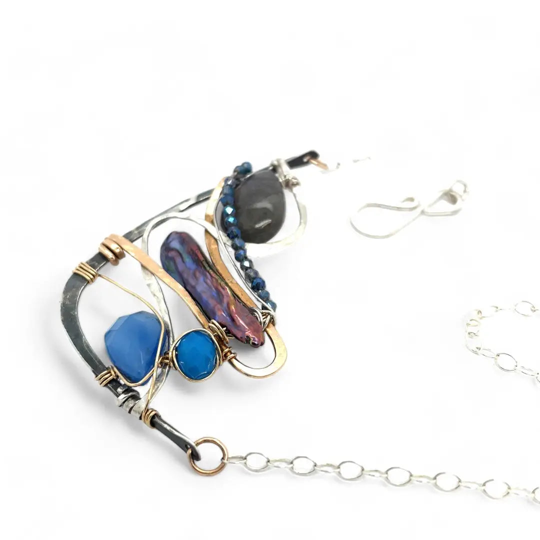 Darkened sterling silver boomerang shaped pendant necklace with waves of hammered bronze, sterling silver, and gold filled wire holding smooth labradorite, blue jade, blue crystal, and a purple fresh water stick pearl in place