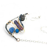 Darkened sterling silver boomerang shaped pendant necklace with waves of hammered bronze, sterling silver, and gold filled wire holding smooth labradorite, blue jade, blue crystal, and a purple fresh water stick pearl in place